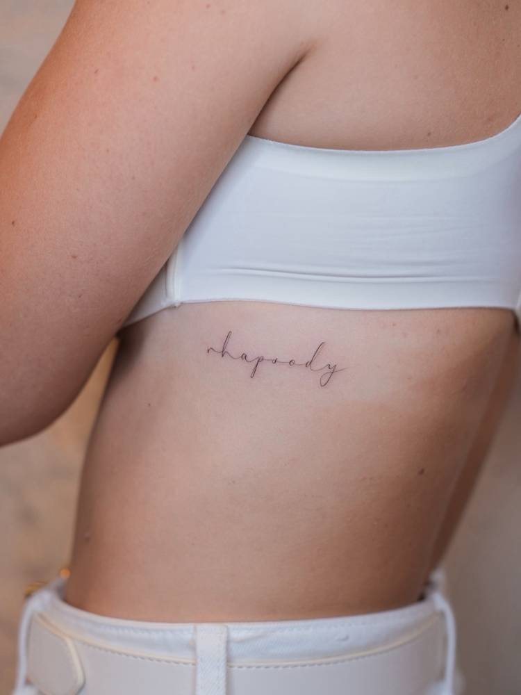 "Rhapsody" lettering tattoo placed on the rib.