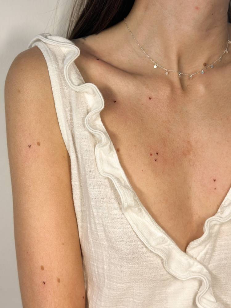 Heart freckles tattooed on the upper arm and chest, minimalistic style.