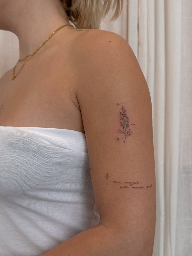 Flower branch and "the magic will never end" tattoos located on the upper arm.