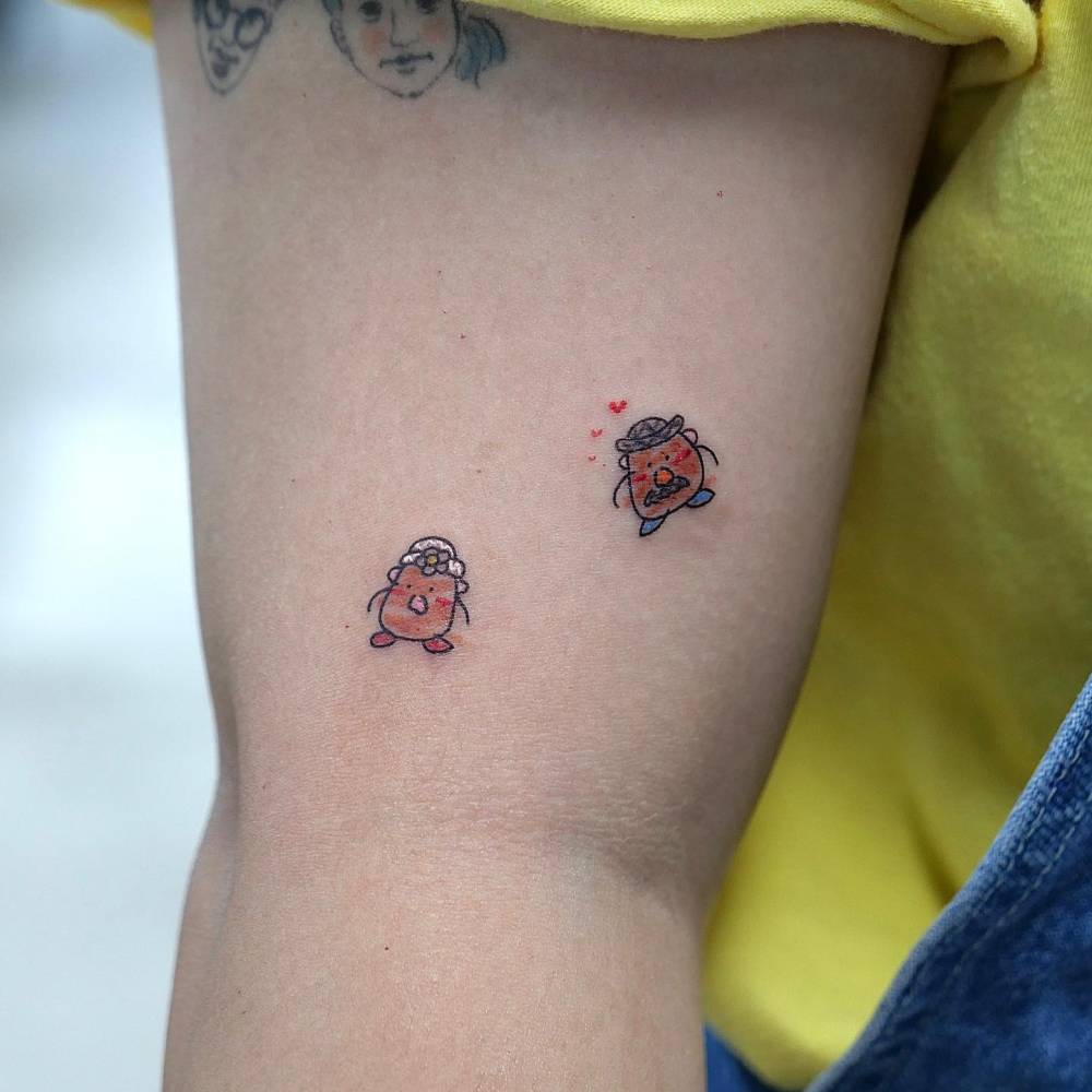 Mr and Mrs Potato Head tattooed on the upper arm, cartoon style.