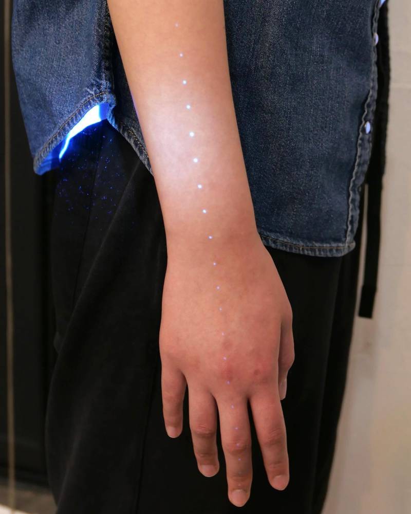UV ink dots tattoo located on the hand and forearm.