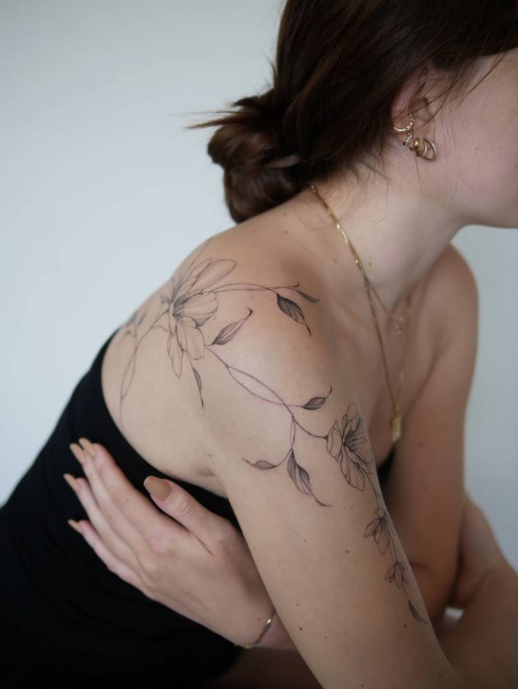 Floral composition tattooed on the shoulder, illustrative style.