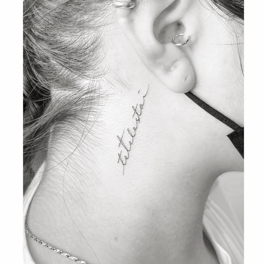 "Tetelestai" lettering tattoo in handwritten font located on the neck.