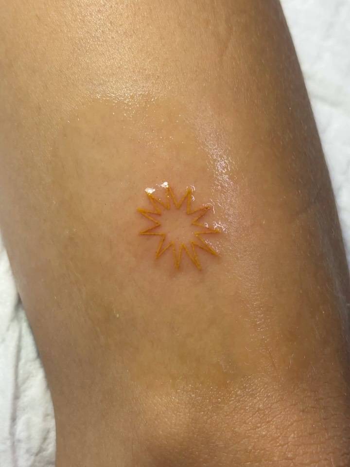 Tiny sun tattoo in minimalistic style located on the tricep.