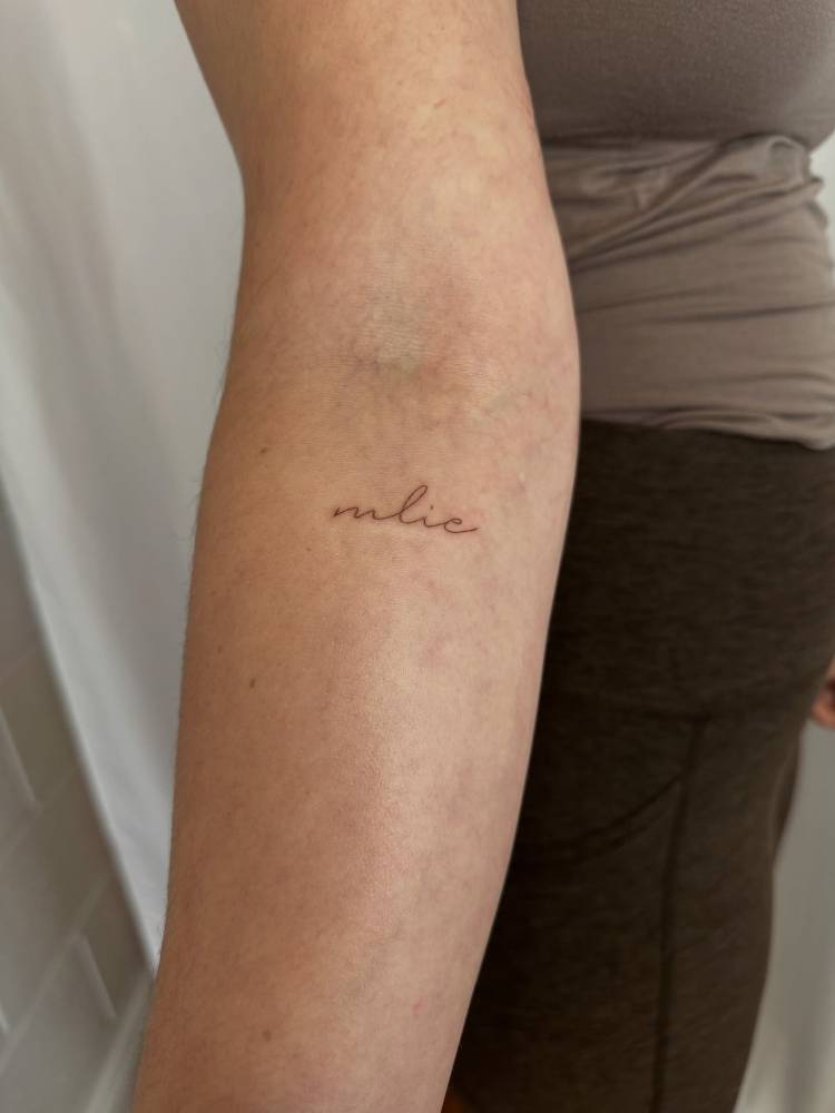 "Mlie" lettering tattoo located on the inner forearm.