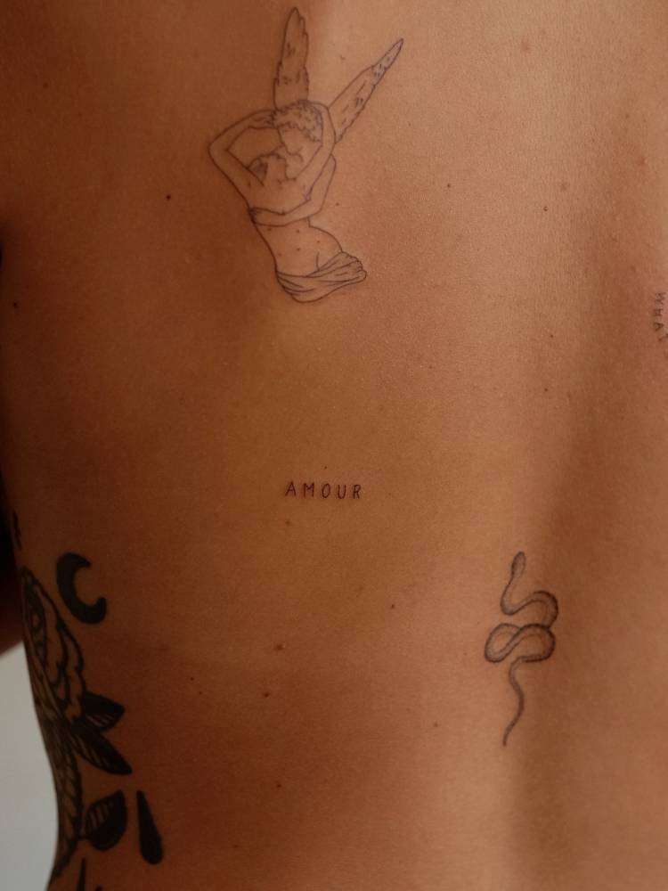Handwritten font word "amour" tattooed on the back.