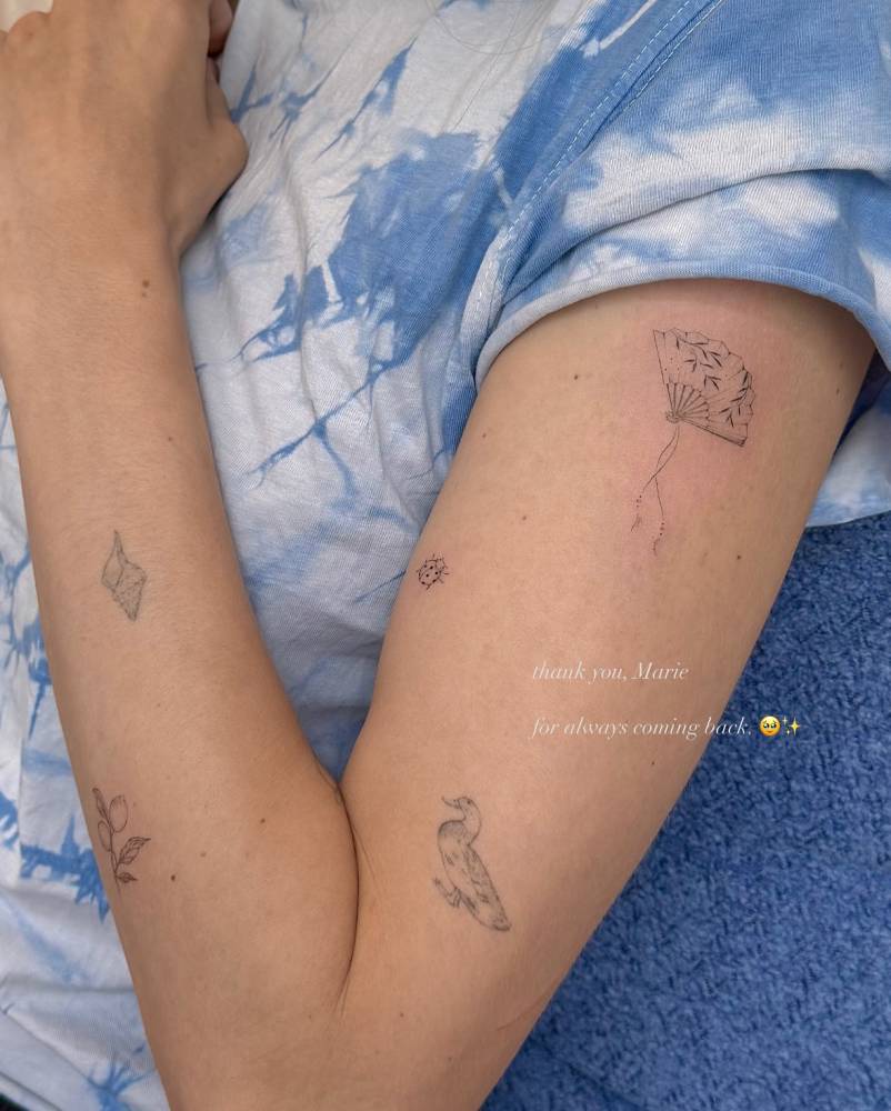 Hand fan tattoo in fine line style located on the upper arm.