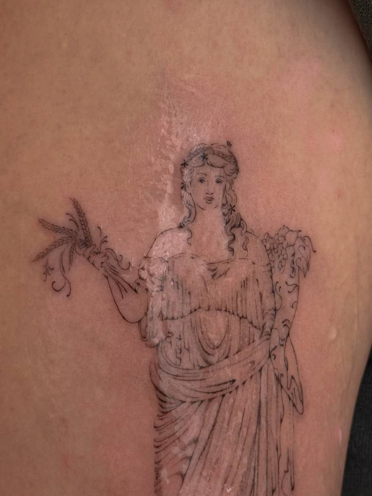 Demeter tattoo located on the thigh, illustrative style.