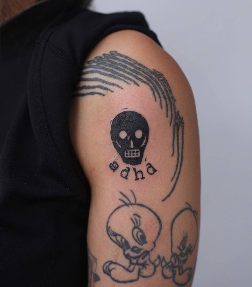 Skull and "ADHD" tattoo located on the upper arm.