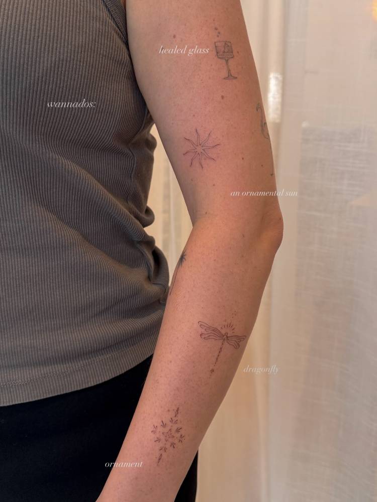 Fine line style ornament, dragonfly and sun tattoos located on the arm.