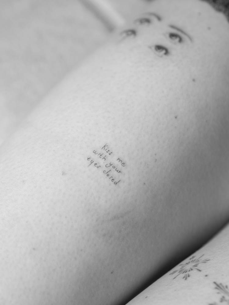 "Kiss me with your eyes closed" lettering tattoo handwritten on the thigh.