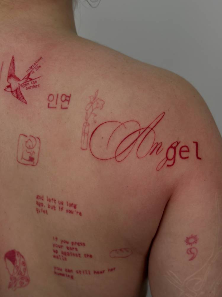 Script font word "angel" in red ink tattooed on the shoulder blade.