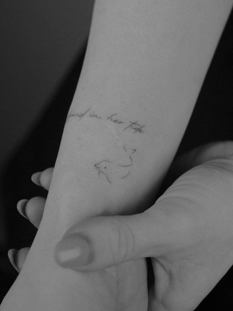 Tiny minimalistic dolphin tattoo located on the wrist.