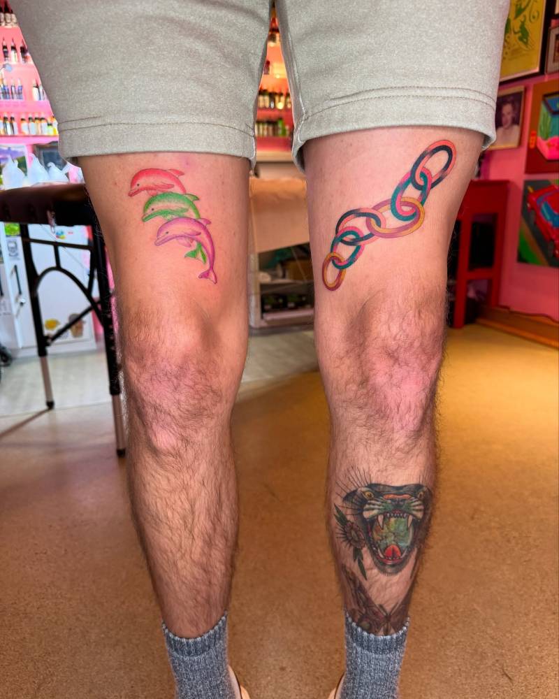 Dolphins and chain tattoos located on the thighs, illustrative style.