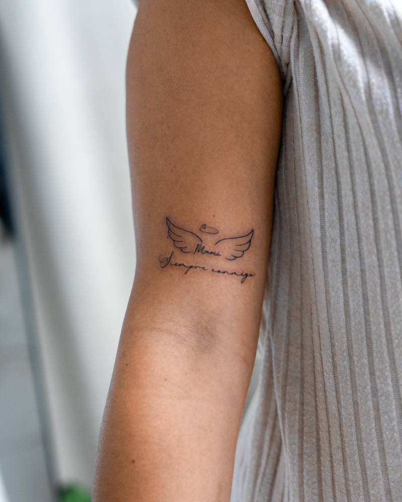Angel wings and halo and "siempre conmigo" tattoo located on the bicep.