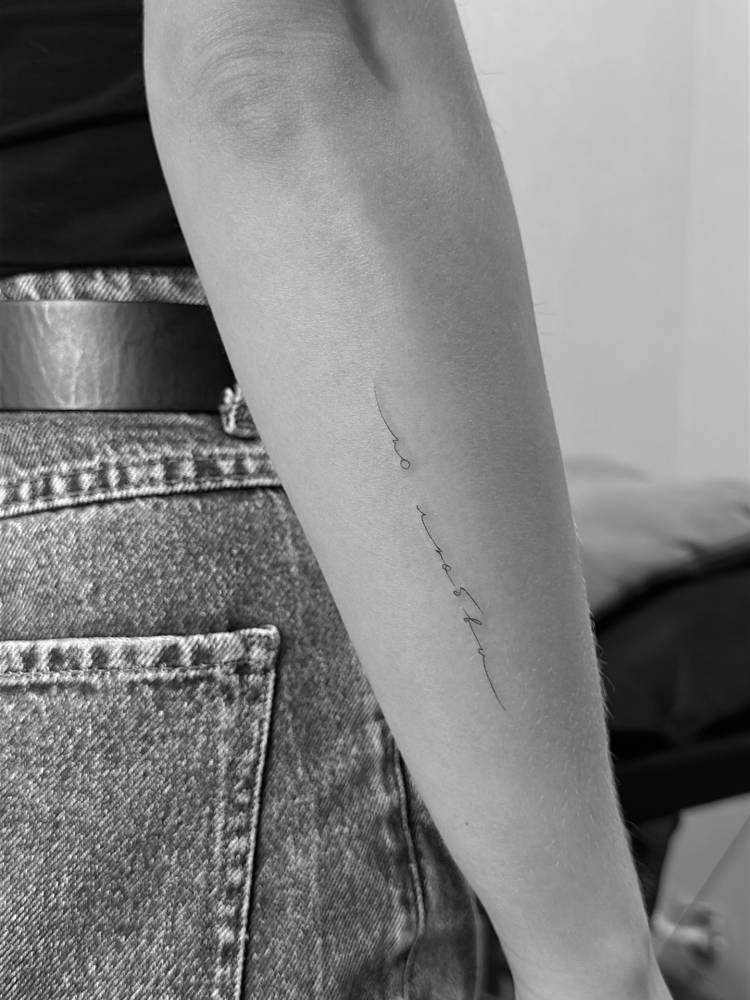 Lettering tattoo in handwritten font located on the forearm.