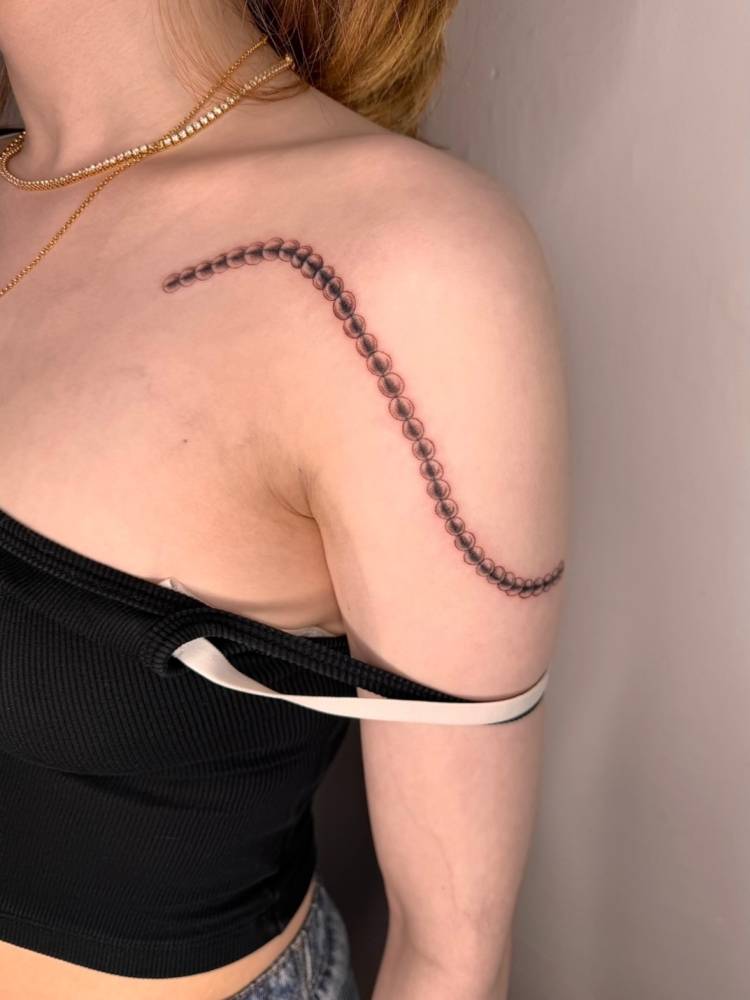 Rosary beads tattoo located on the shoulder, illustrative style.