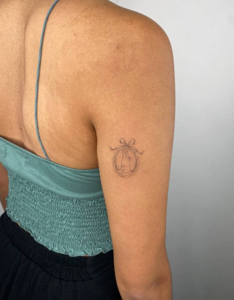 Rabbit pendant tattoo located on the tricep, illustrative style.