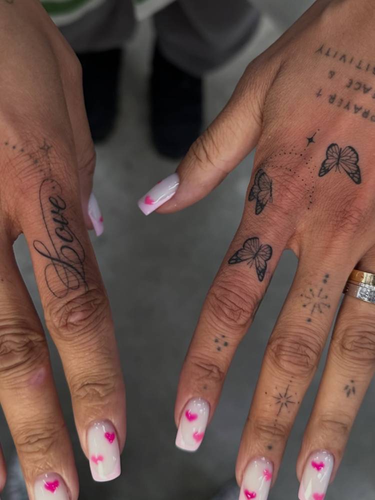 Word "love" and butterflies tattoo located on the fingers and hand.
