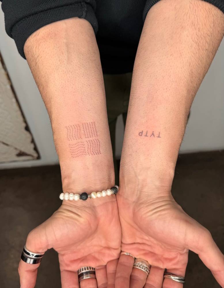 Dotted lines and initials tattoos located on the wrists.