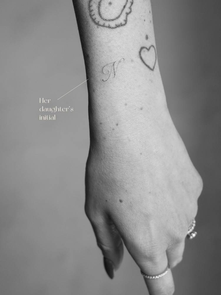 Script font letter "N" tattoo located on the wrist.