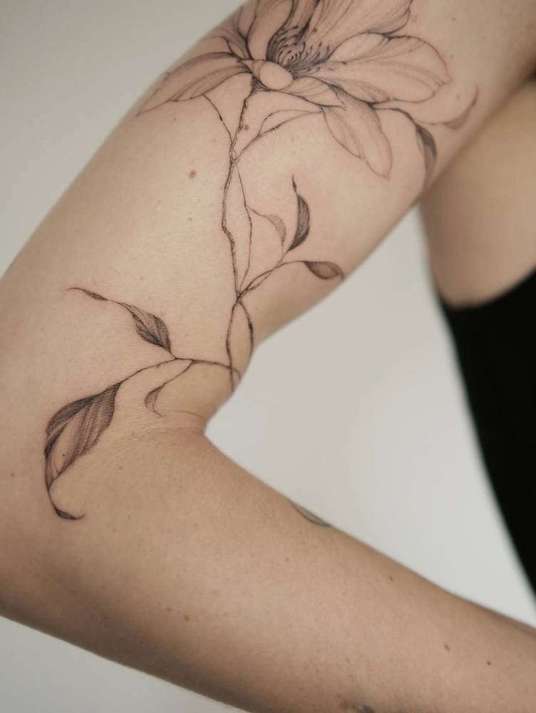 Magnolia flower tattoo in illustrative style located on the upper arm.