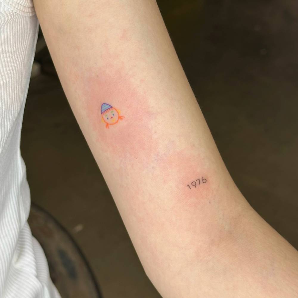 Hand poked minimalist snowman face and "1976" tattoos.