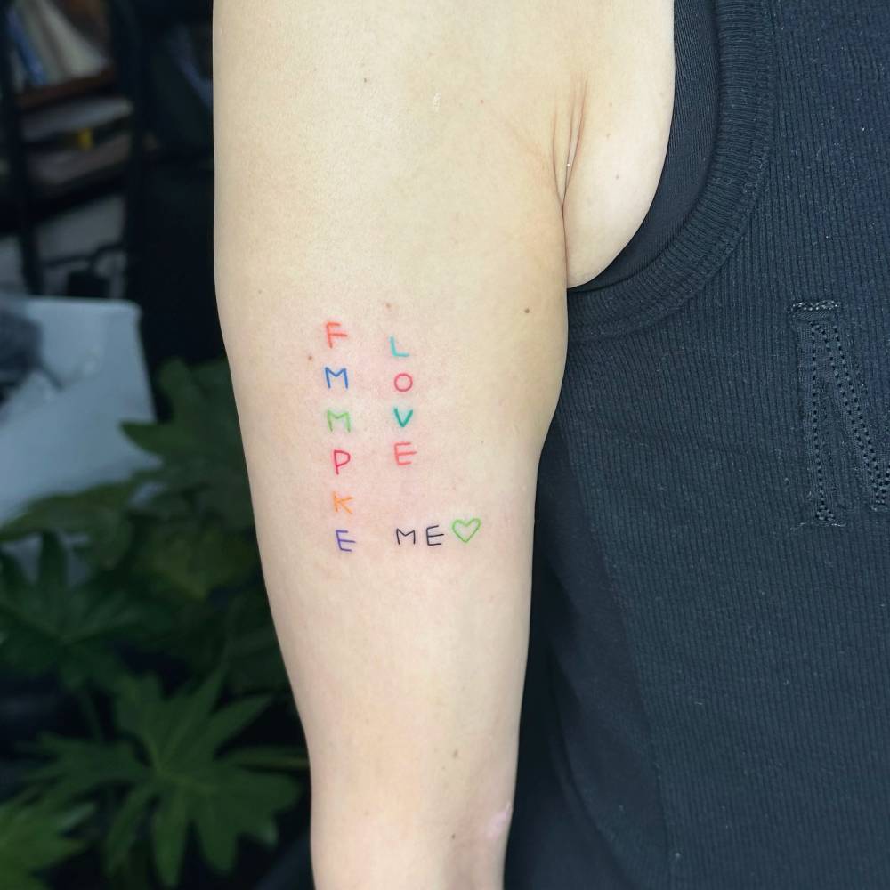 Word "love me" and initials tattoo hand poked on the upper arm.