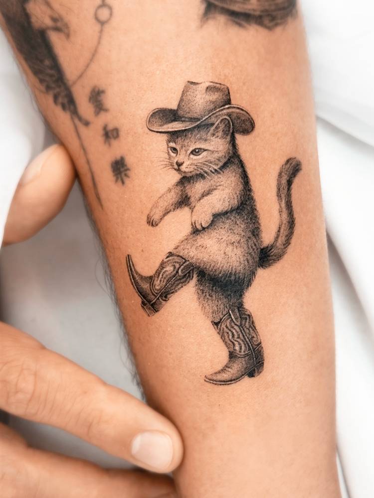 Cowboy cat tattoo located on the forearm, micro-realistic style.