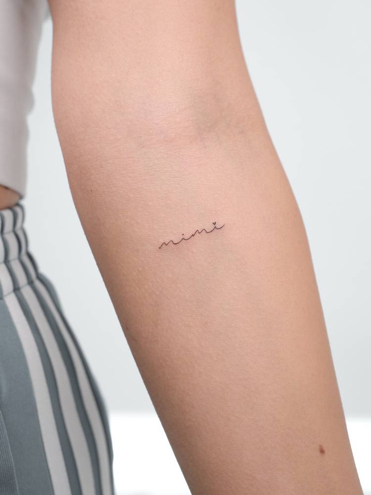 Handwritten font "Mimi" lettering tattoo located on the inner forearm.
