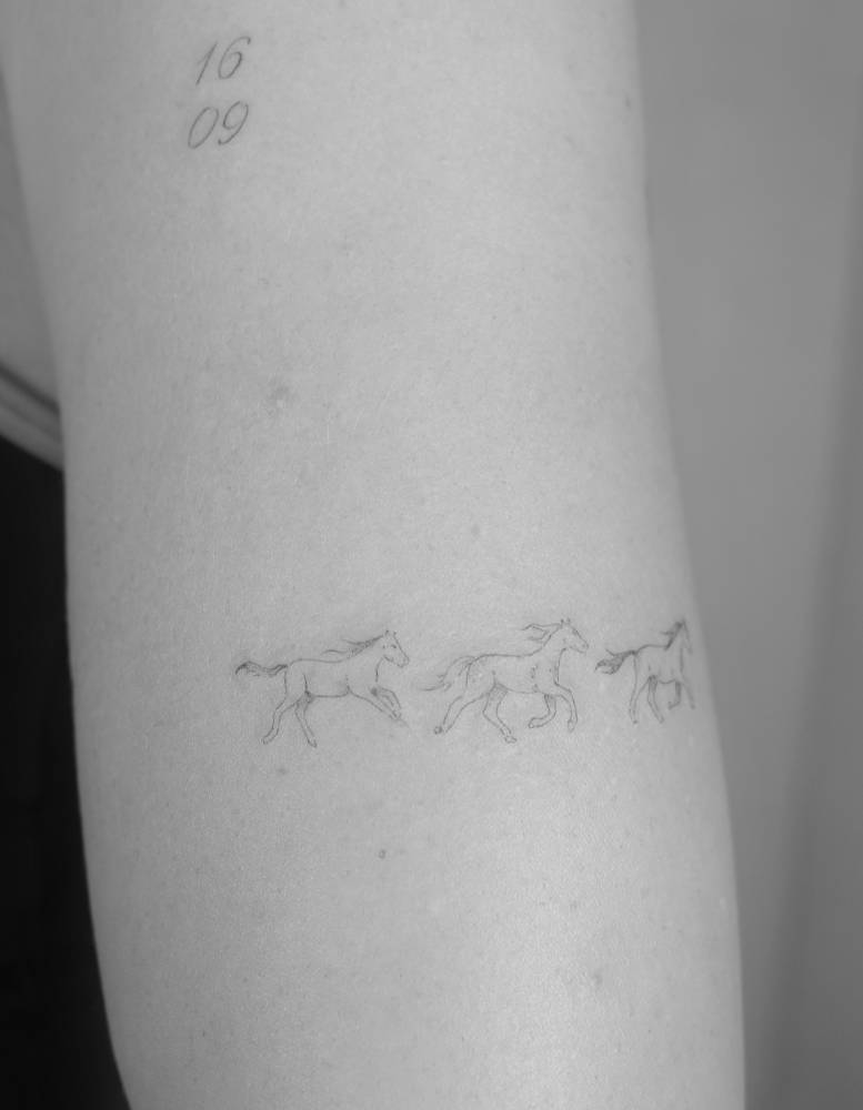 Running horses tattoo in fine line style done on the upper arm.
