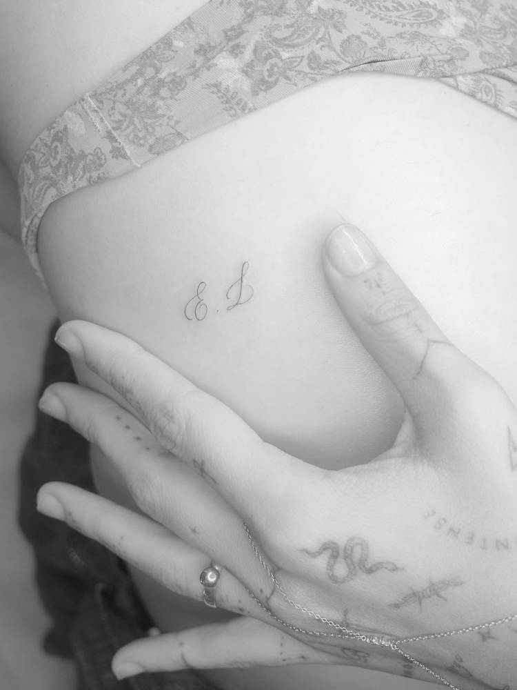 Initials tattoo located on the rib, script font.
