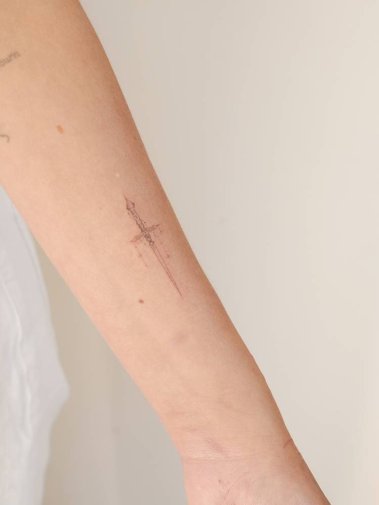 Dagger tattoo located on the inner forearm, fine line style.