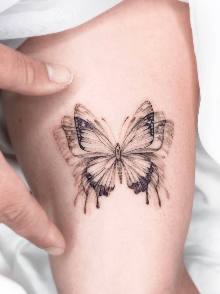 Flying butterfly tattoo located on the inner arm, illustrative style.