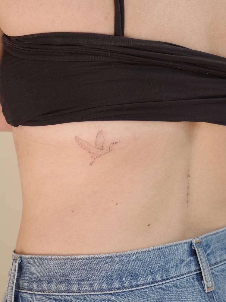 Little crane tattoo located on the back, fine line style.