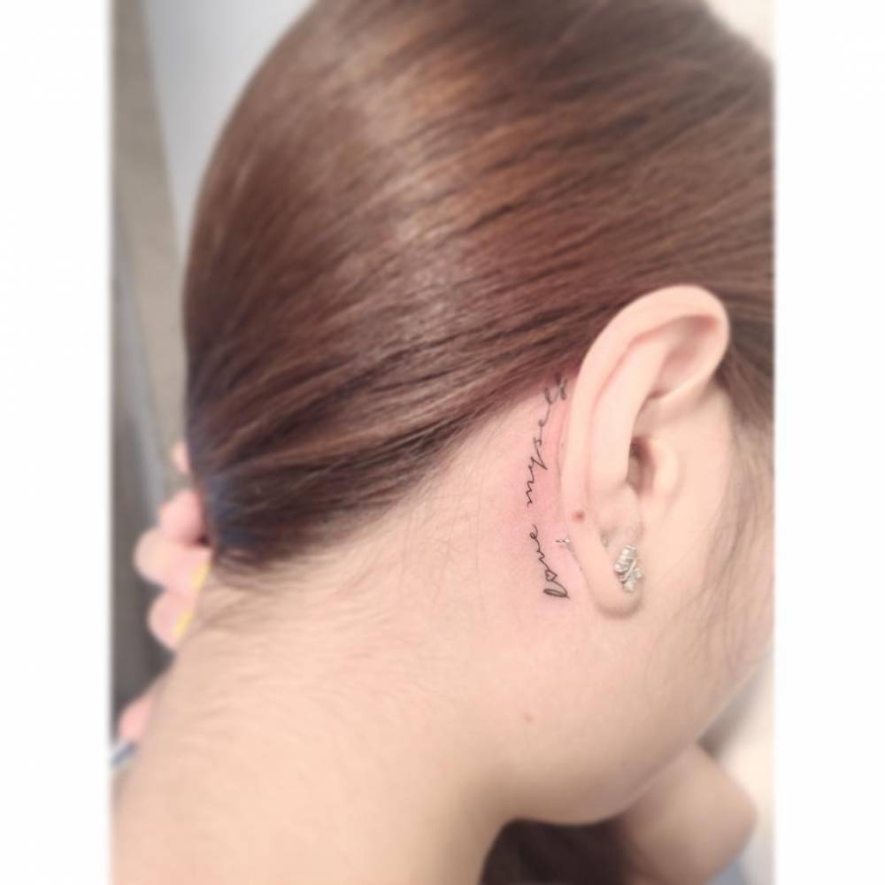 Handwritten font "love myself" lettering tattoo located behind the ear.