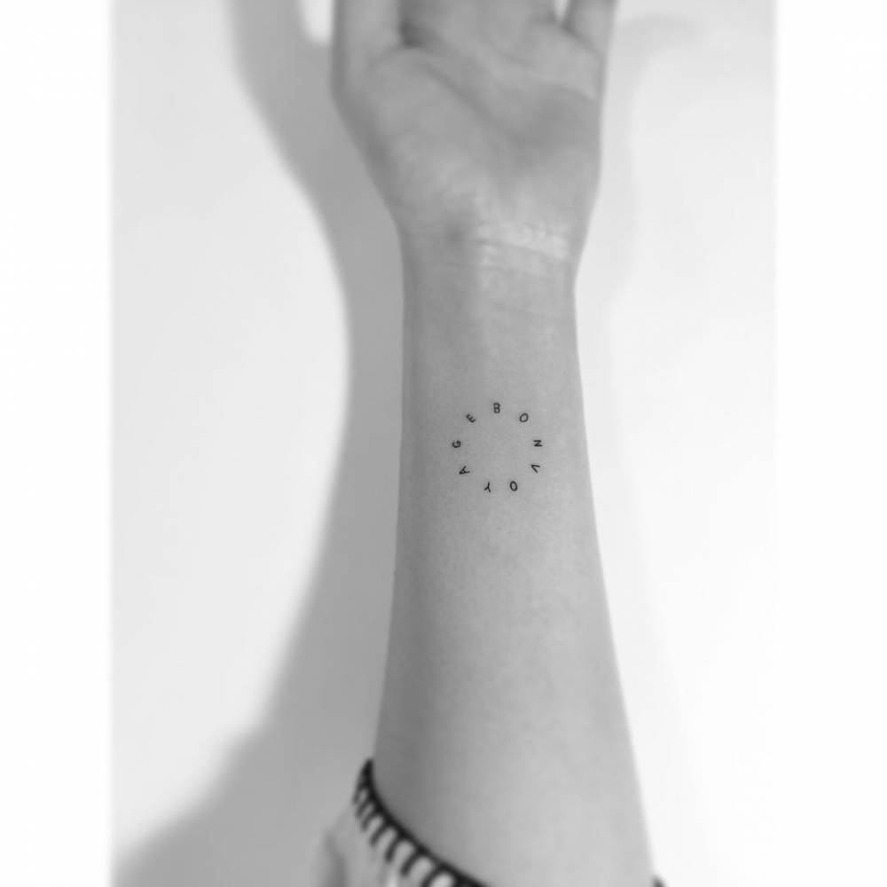 "Bon voyage" lettering tattoo in circle located on the wrist.