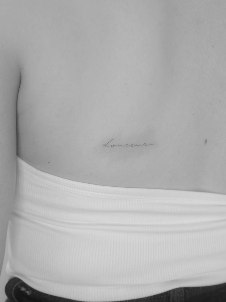 "Douceur" lettering tattoo in handwritten font placed on the back.