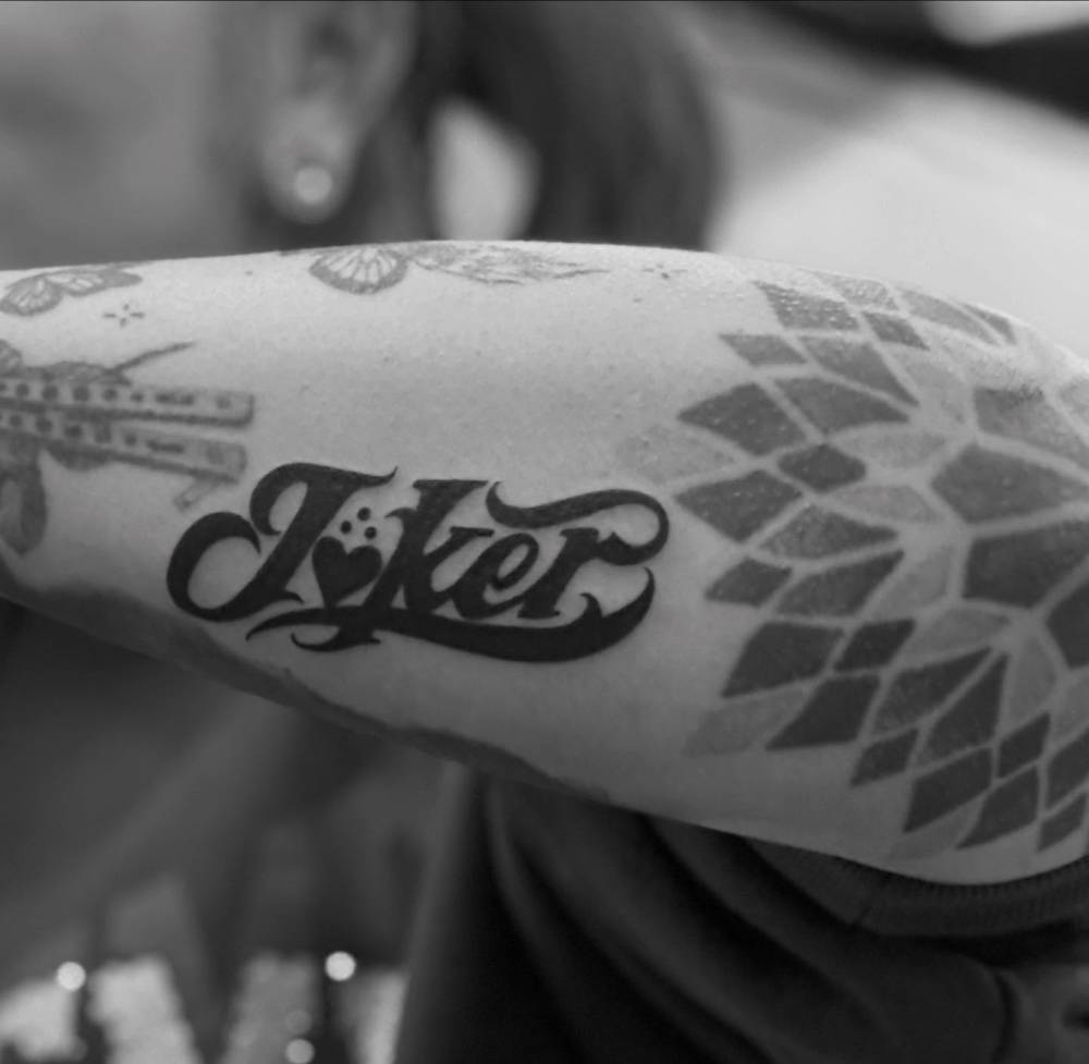 Lettering tattoo of the word "joker" located on the forearm.