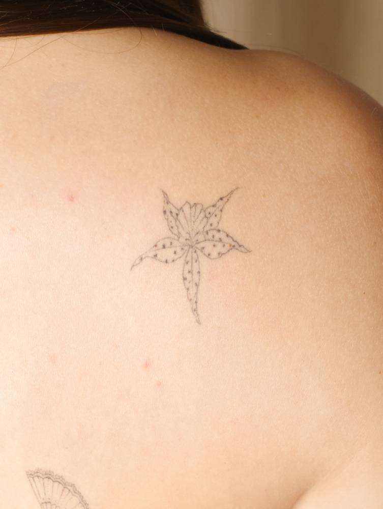 Little orchid tattoo in fine line style located on the shoulder blade.