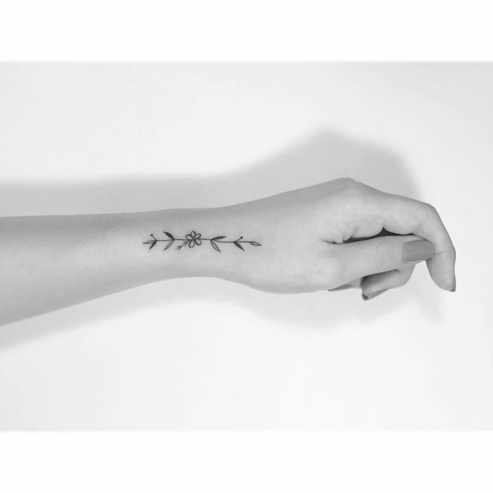 Minimalistic style flower tattoo located on the wrist.