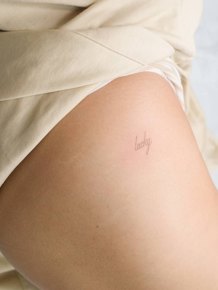 Script font word "lucky" tattoo located on the rib.