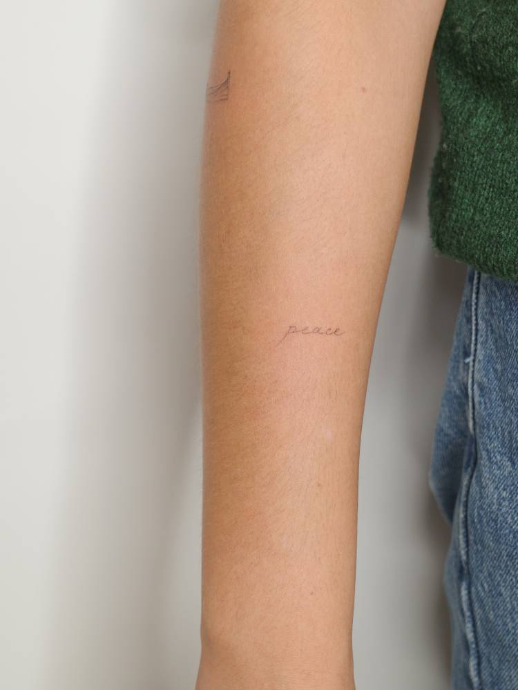Handwritten font word "peace" tattoo done on the forearm.