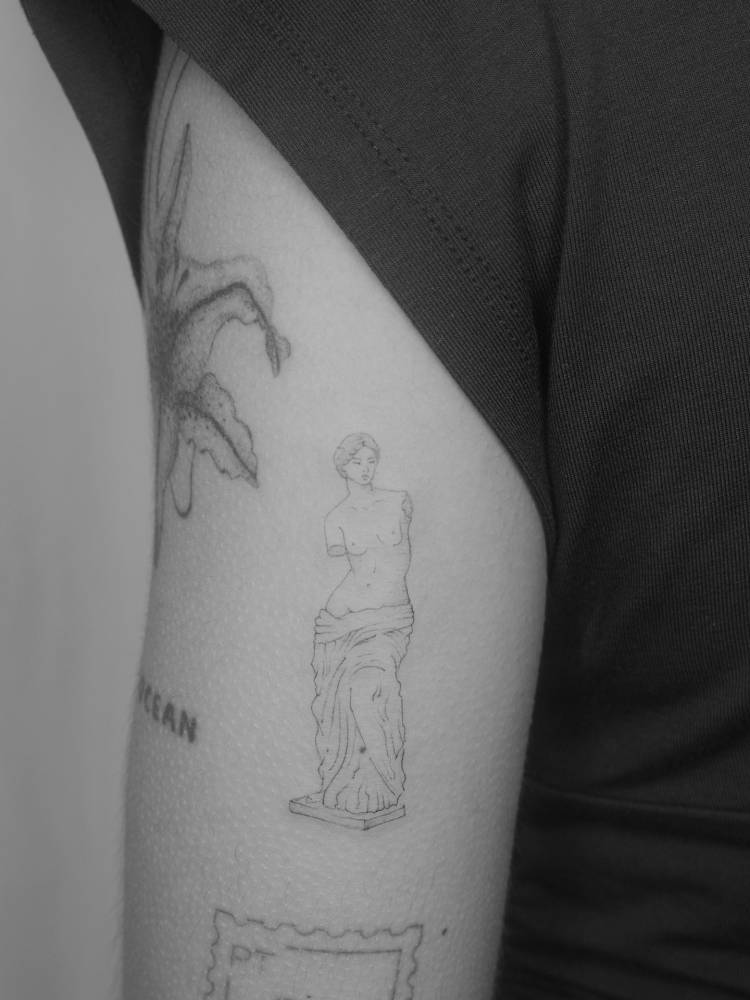 Fine line style Venus de Milo tattoo located on the tricep.