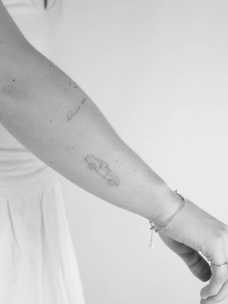 Small car tattoo located on the forearm, done in fine line style.