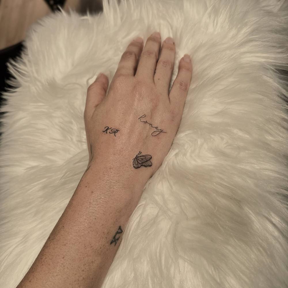 Word "honey", butterfly and initials tattooed on the hand.