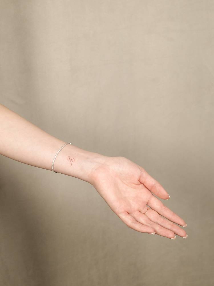 Little letter "E" tattoo in script font located on the wrist.