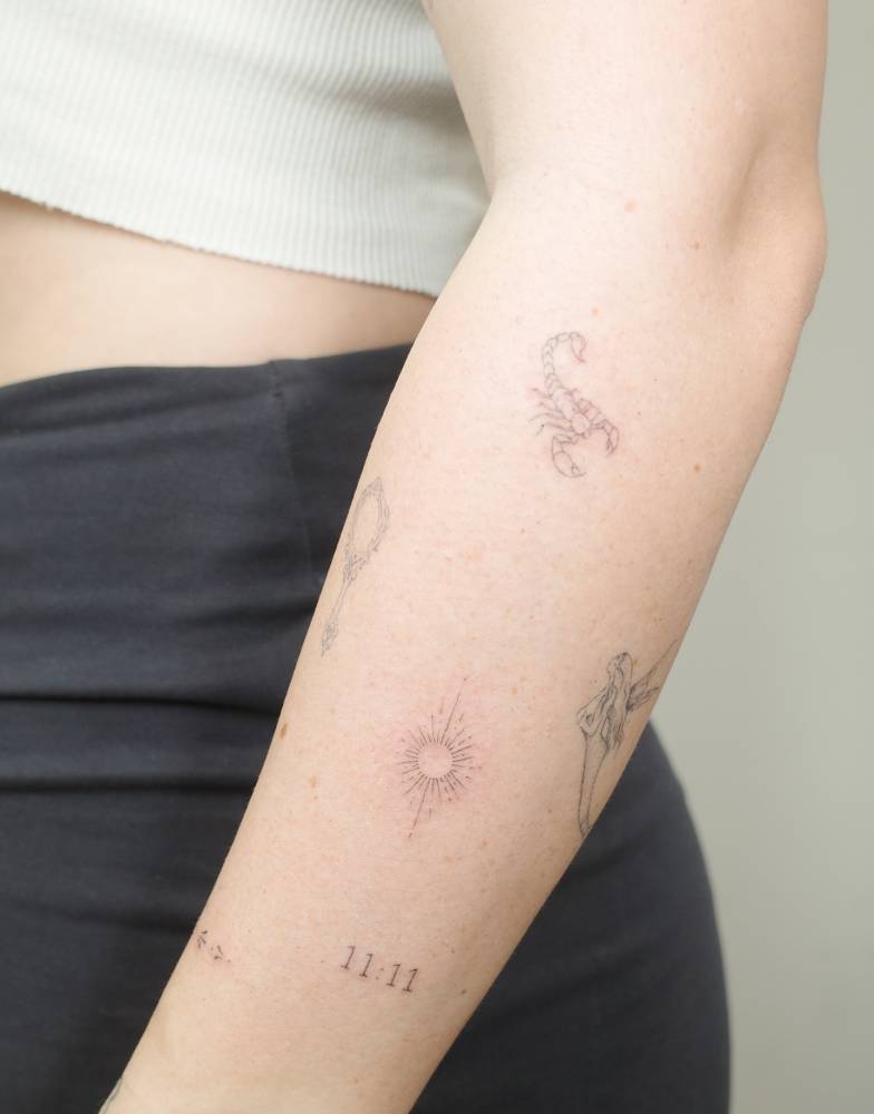 Scorpion and sun tattoos located on the forearm, done in fine line style.