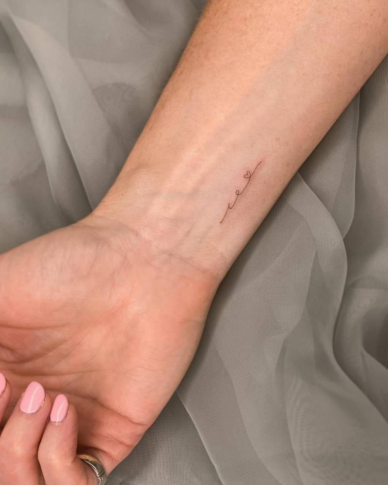 Handwritten font initials and heart tattoo located on the wrist.