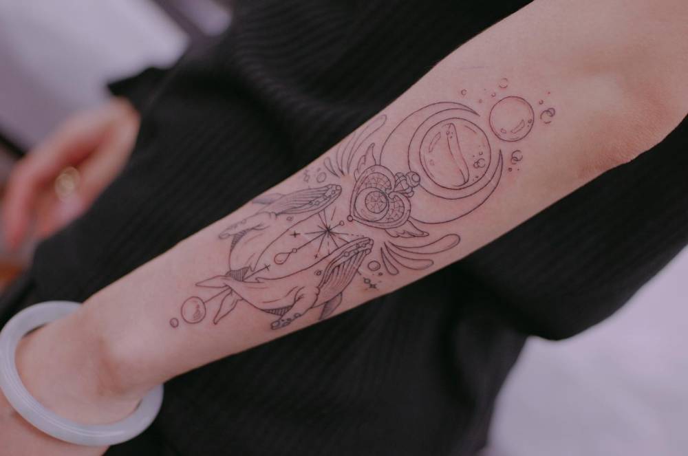 Fine line style whales and Moon Crisis tattoo located on the forearm.